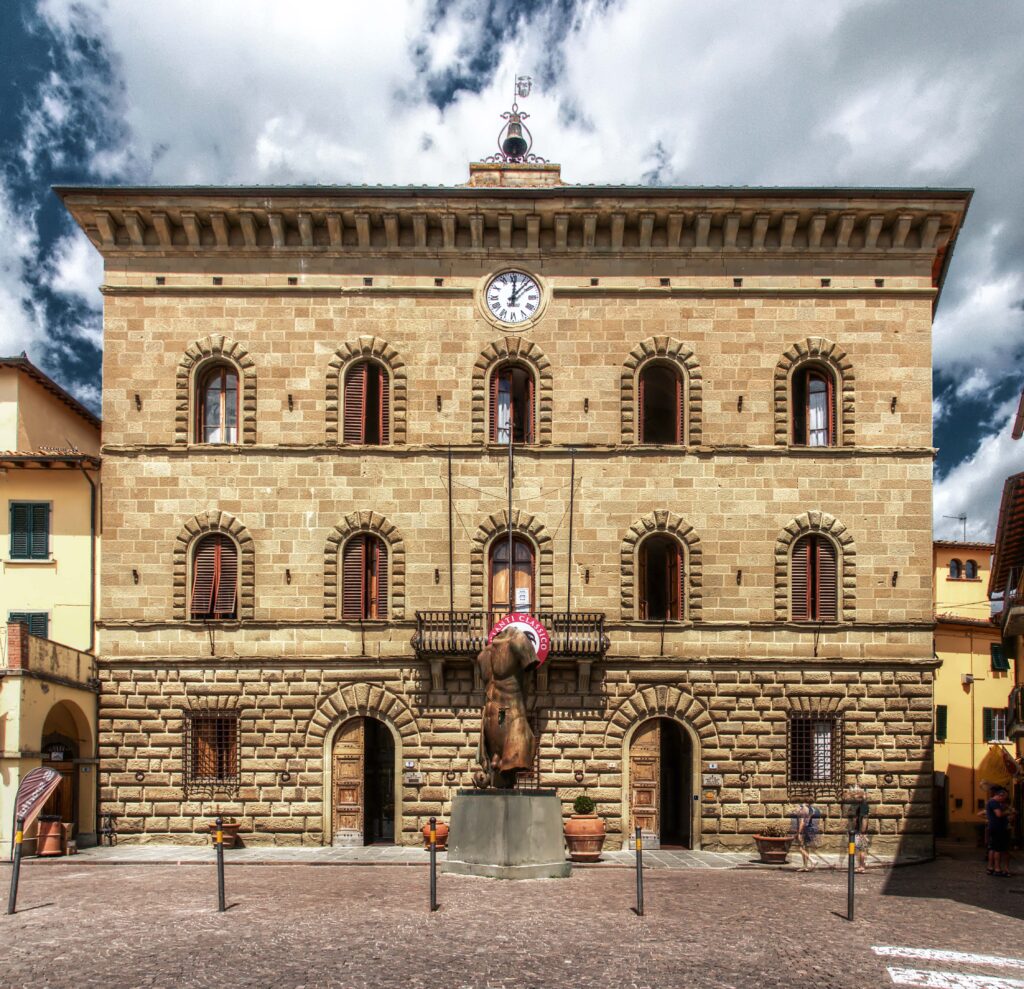 Montepulciano, Italy: Palazzo Comunale, a historic stone building with a clock, statue, and arched windows.